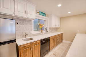 Kitchen with freestanding refrigerator, black dishwasher, backsplash, light countertops, and recessed lighting