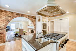 Kitchen with appliances with stainless steel finishes, extractor fan, dark stone countertops, arched walkways, and light wood-style floors