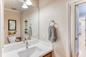 Half bathroom featuring ornamental molding, vanity, and wood finished floors
