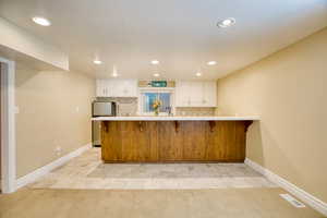 Kitchen featuring a breakfast bar area, fridge, white cabinets, light countertops, and recessed lighting