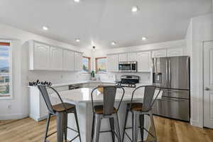 Kitchen featuring stainless steel appliances, a kitchen breakfast bar, white cabinetry, light wood-type flooring, and recessed lighting