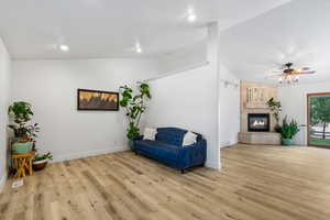 Sitting room with vaulted ceiling, wood finished floors, a ceiling fan, recessed lighting, and a tiled fireplace
