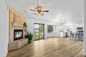 Unfurnished living room featuring healthy amount of natural light, a fireplace, a chandelier, light wood finished floors, and vaulted ceiling