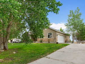 View of property hidden behind natural elements with stucco siding, concrete driveway, a garage, a front yard, and stone siding