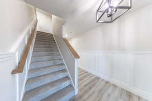 Stairway with wood finished floors, wainscoting, a chandelier, and a decorative wall