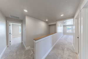Hallway featuring carpet floors, a textured ceiling, recessed lighting, and an upstairs landing