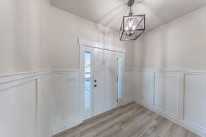 Entrance foyer with a decorative wall, light wood-type flooring, a chandelier, and wainscoting