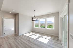 Unfurnished dining area featuring light wood-type flooring, a chandelier, and a textured ceiling