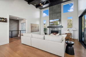 Living room featuring a towering ceiling, wood finished floors, plenty of natural light, a tile fireplace, and a wooden ceiling with exposed beams