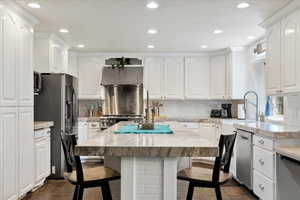 Kitchen with stainless steel refrigerator with ice dispenser, a kitchen breakfast bar, white cabinets, and recessed lighting