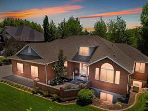 View of front of property featuring brick siding, a shingled roof, a lawn, and a patio area