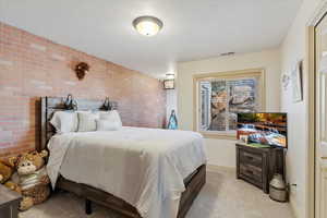 Bedroom with brick wall and light colored carpet