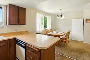 Kitchen with white dishwasher, a peninsula, light countertops, and a chandelier