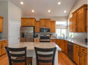 Kitchen featuring appliances with stainless steel finishes, lofted ceiling, light wood finished floors, a kitchen island, and light stone counters