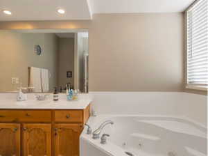 Full bath featuring a tub with jets, vanity, and recessed lighting
