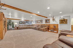 Carpeted living room with recessed lighting, beam ceiling, wainscoting, and wooden walls