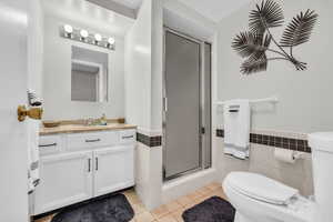 Bathroom with toilet, tile patterned floors, tile walls, vanity, and a shower stall