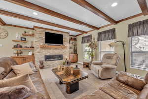 Carpeted living area with beam ceiling, crown molding, a stone fireplace, baseboards, and recessed lighting