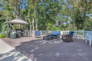 Pool area. Wooden deck with an outdoor hangout area, area for grilling, a gazebo, and view of scattered trees