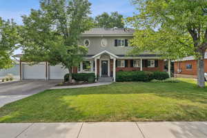 Colonial home with driveway, a front yard, brick siding, stucco siding, and a garage