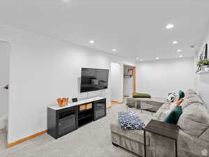 Living room with recessed lighting and carpet floors. Hall shown to door of  large storage/utility room and small room to play, finished under the stairs backing this tv wall.