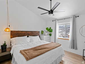 Primary bedroom with light wood-style floors, lofted ceiling with fan, and backyard view of private yard and nature galore!