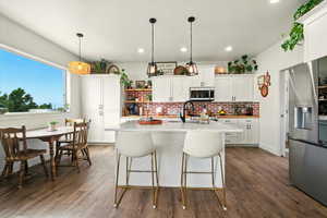 Kitchen featuring appliances with stainless steel finishes, backsplash, light countertops, dark wood-style floors, and an island with sink