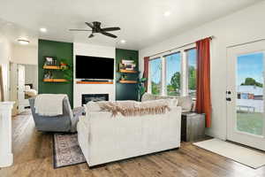 Living room with ceiling fan, a glass covered fireplace, wood finished floors, and recessed lighting