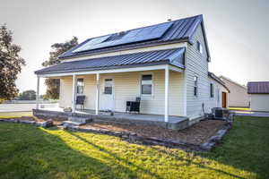 View of front of home featuring covered porch, solar panels, a front yard, and a metal roof