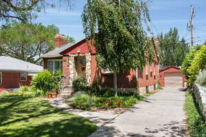 Bungalow with a garage, a chimney, an outbuilding, a front lawn, and brick siding