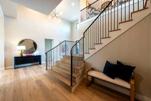 Staircase with a towering ceiling, a chandelier, and wood finished floors