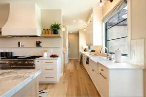 Kitchen with double oven range, custom range hood, light wood-type flooring, white cabinetry, and tasteful backsplash