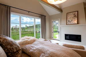 Bedroom with access to outside, a glass covered fireplace, and high vaulted ceiling