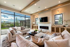 Living room featuring a glass covered fireplace, light wood-style floors, recessed lighting, and beam ceiling