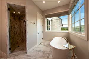 Bathroom featuring a freestanding tub, recessed lighting, a marble finish shower, and marble look tile flooring