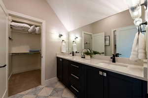 Bathroom featuring double vanity, lofted ceiling, and a spacious closet