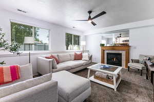 Carpeted living room with a ceiling fan, a fireplace, and a textured ceiling