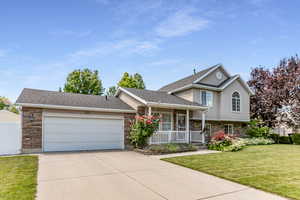 Split level home featuring stone siding, a porch, a front yard, concrete driveway, and an attached garage