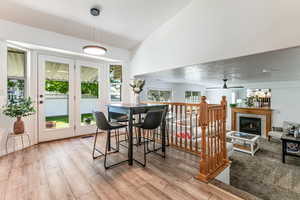 Dining area featuring a fireplace, plenty of natural light, ceiling fan, light wood-style floors, and high vaulted ceiling