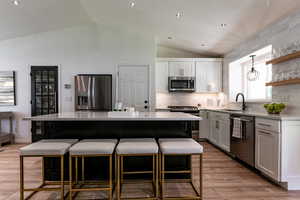 Kitchen with appliances with stainless steel finishes, vaulted ceiling, a kitchen breakfast bar, a kitchen island, and light countertops