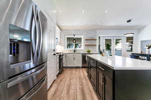 Kitchen with stainless steel appliances, white cabinets, light countertops, light wood-type flooring, and hanging light fixtures