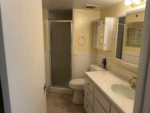 Full bathroom featuring toilet, a wainscoted wall, vanity, a stall shower, and a textured ceiling