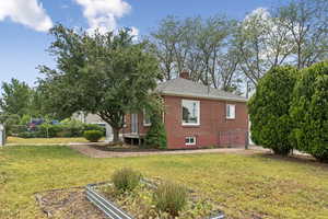 View of side of property with brick siding, a chimney, a vegetable garden, and roof with shingles