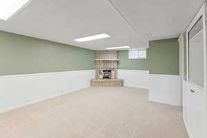 Basement with a wainscoted wall, carpet flooring, a brick fireplace, and a textured ceiling