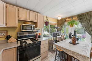 Kitchen with gas range, light brown cabinetry, stainless steel microwave, and light countertops