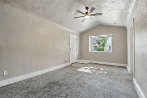 Unfurnished room featuring a textured ceiling, carpet, ceiling fan, and lofted ceiling