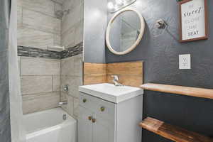 Bathroom with shower / bath combination with curtain, vanity, and a textured wall