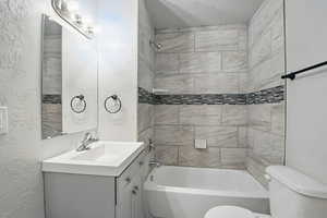 Full bathroom with a textured wall, vanity, shower / bath combination, and a textured ceiling