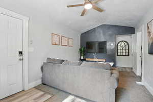 Living area featuring vaulted ceiling, ceiling fan, and a textured ceiling