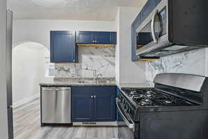 Kitchen featuring appliances with stainless steel finishes, blue cabinetry, tasteful backsplash, light wood-style floors, and arched walkways